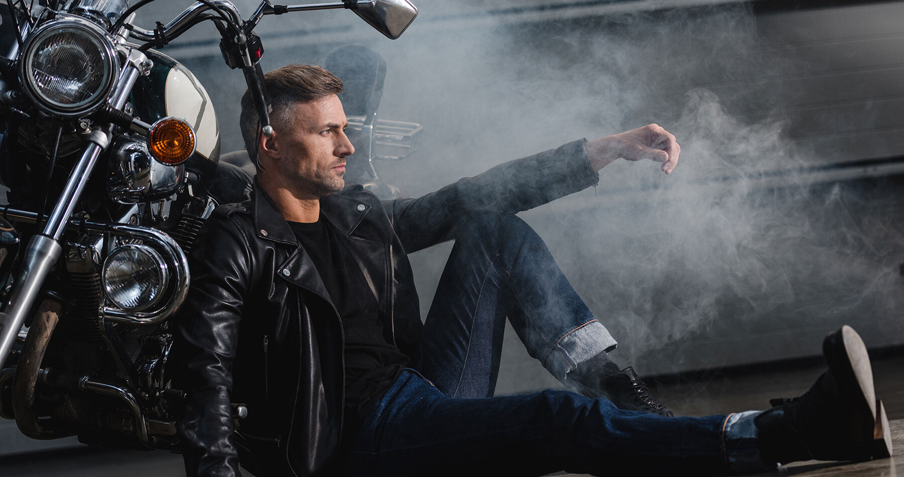 Man in leather jacket sitting on a motorcycle with smoke in the background